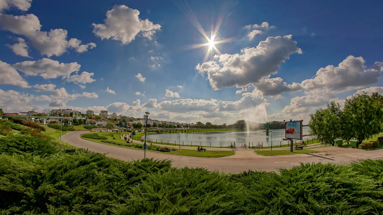 Lake Sava at Ada Ciganlija on a bright summer day, with the central fountain jet, paved paths and the wooded far shore