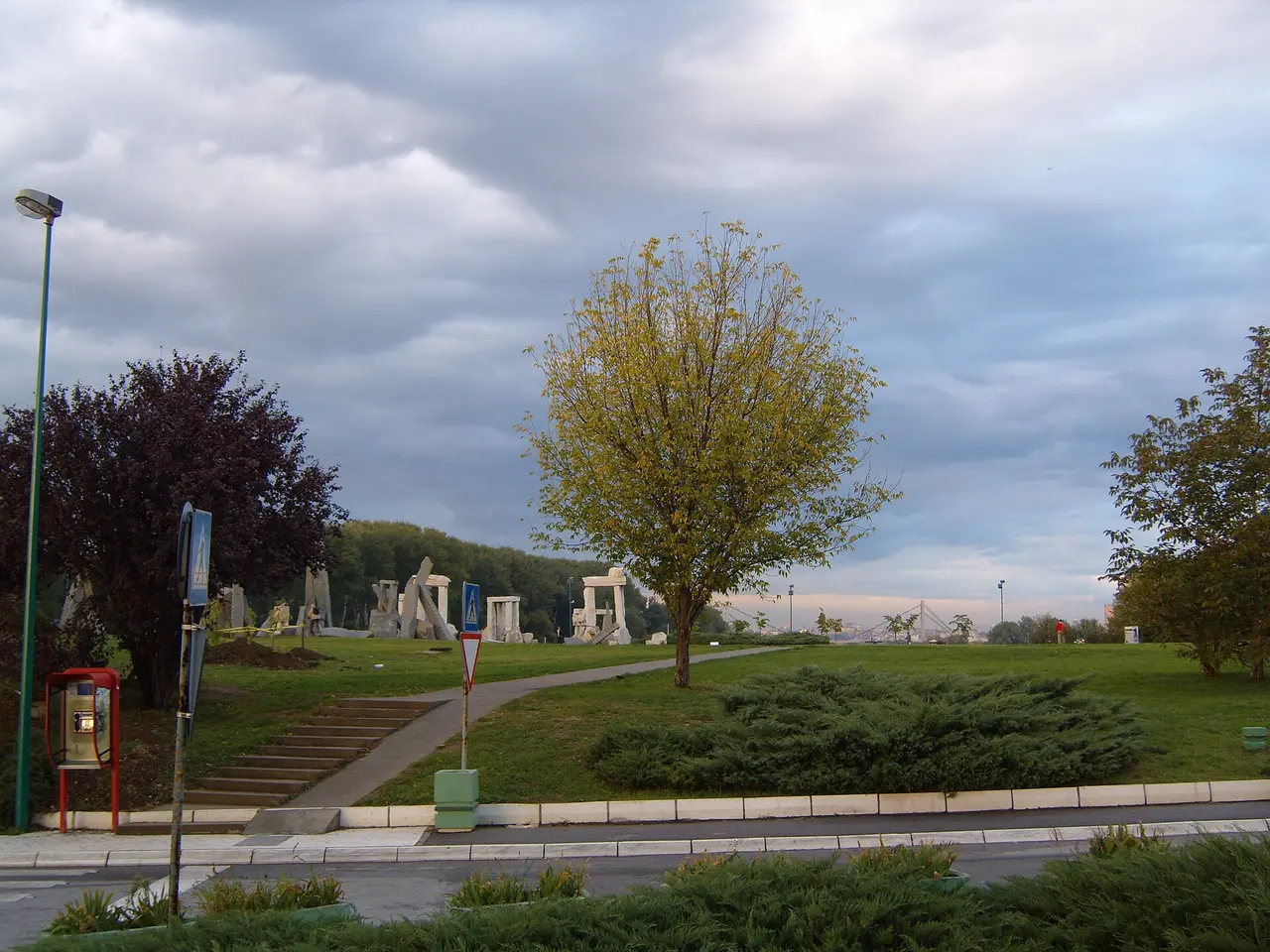 Stone-block sculptures at Kamen Grad on Ada Ciganlija, with the Ada Bridge pylon above the trees