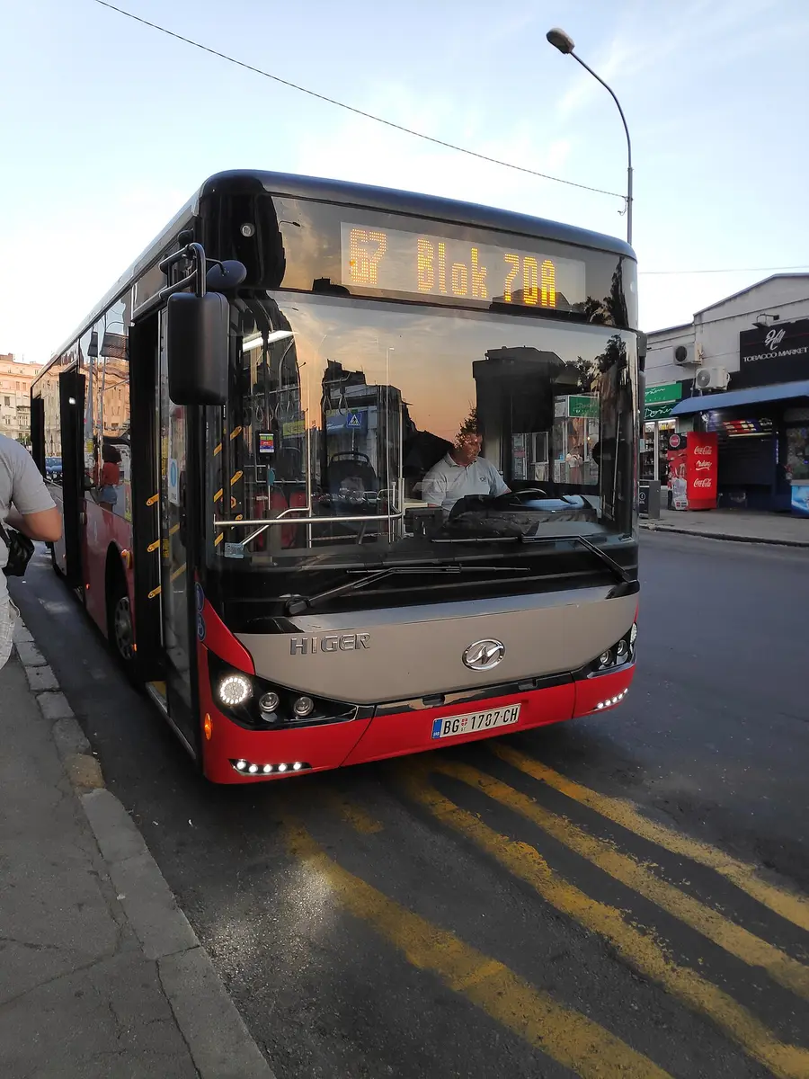 A red-and-white Belgrade city bus at a stop, of the type that runs the free route 72