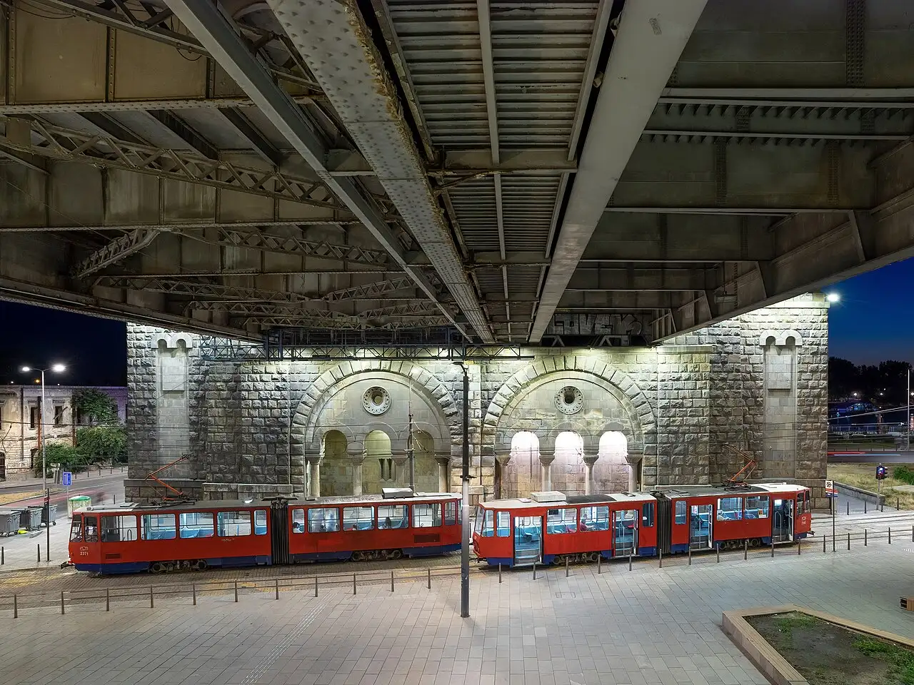 Red trams parked at night under the steel girders of Brankov bridge in Belgrade
