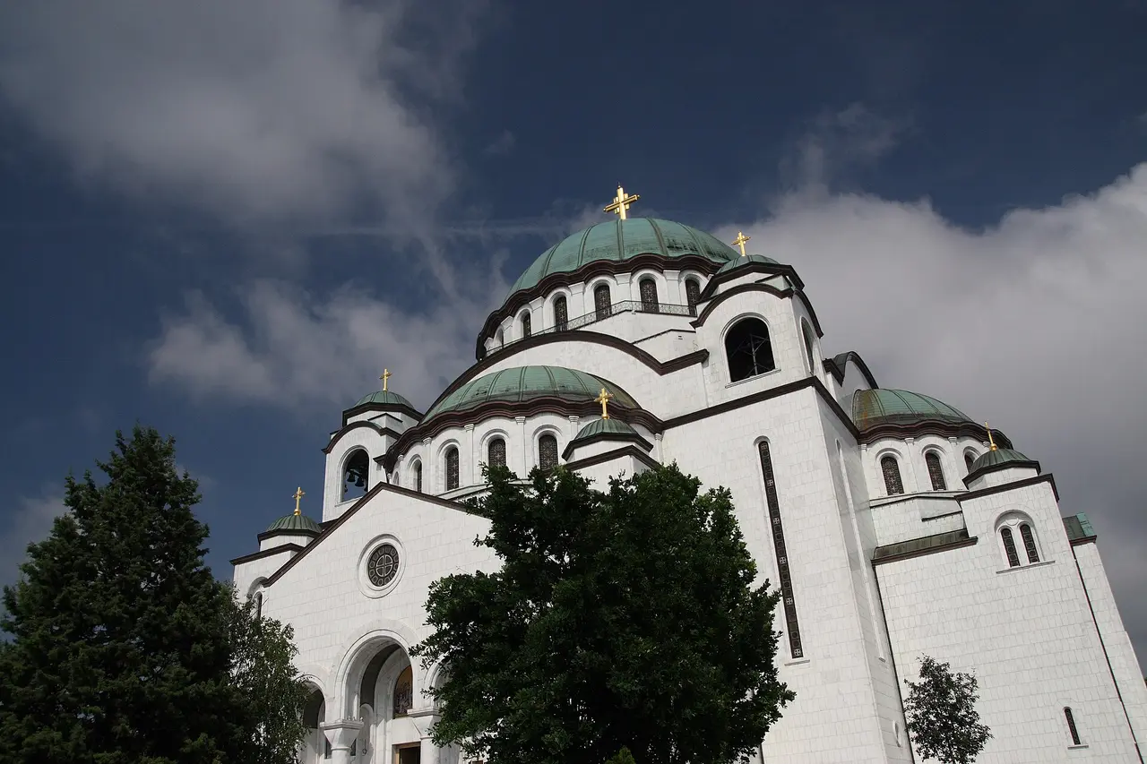 The white marble Temple of Saint Sava in Belgrade with its green domes against a dramatic sky