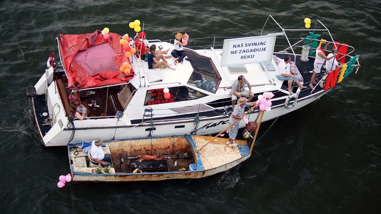 A decorated party boat on the river during Belgrade boat carnival with bridges behind