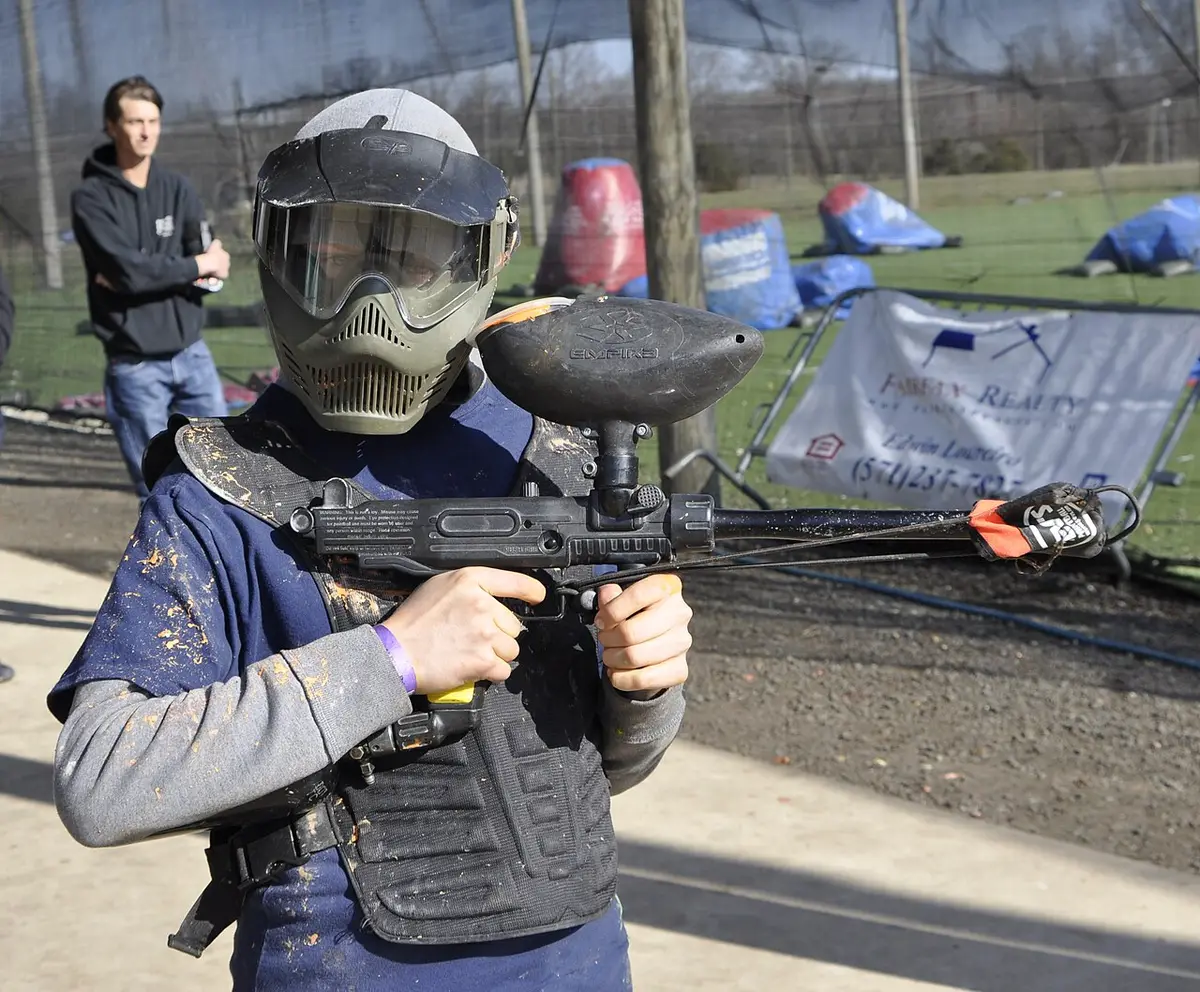 A paintball player in full kit aiming across an outdoor field