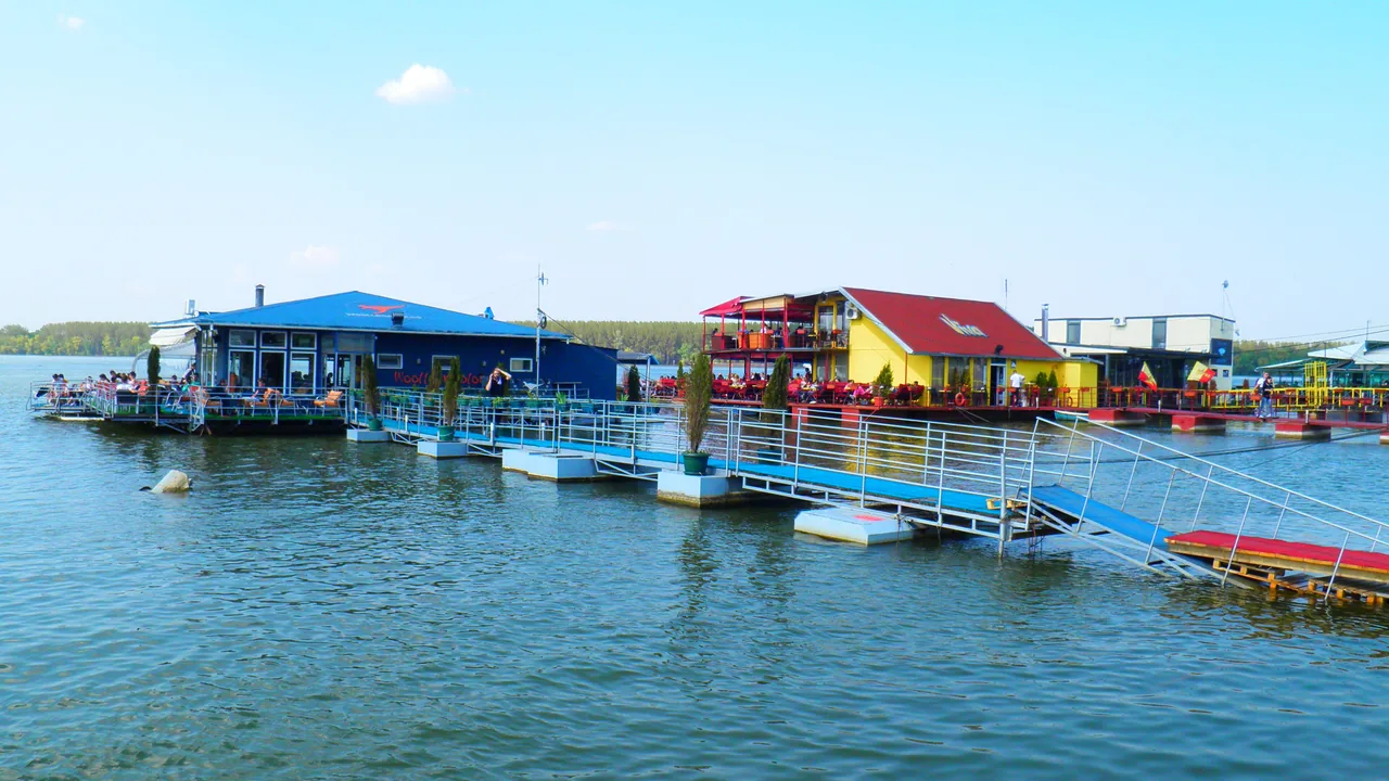A row of brightly painted floating clubs moored on the river in Belgrade, with terraces, gangways and outdoor seating