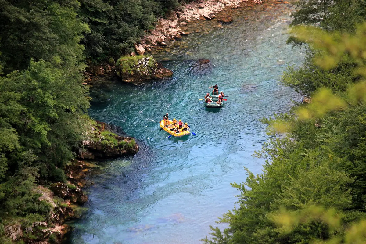 Two rafts full of people running the clear green water of a river canyon, the classic Serbian rafting day out