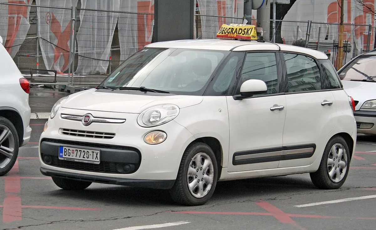A white Fiat 500L Belgrade city taxi with a rooftop taxi sign on a city street