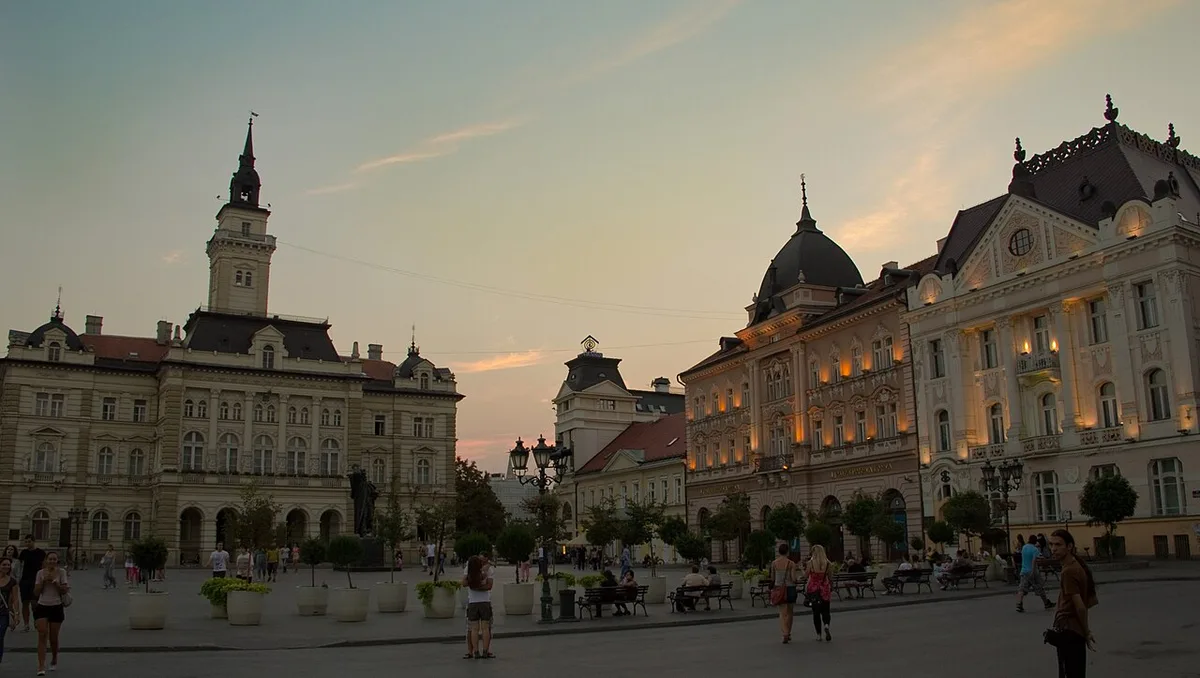 Freedom Square (Trg slobode) in Novi Sad at dusk, with the City Hall tower and the Name of Mary Church buildings