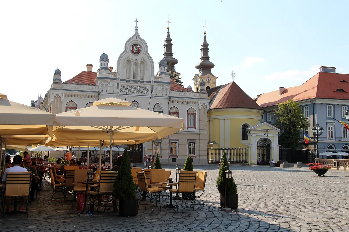 Cafe terraces on Piata Unirii (Union Square) in Timisoara with the Serbian Orthodox church behind