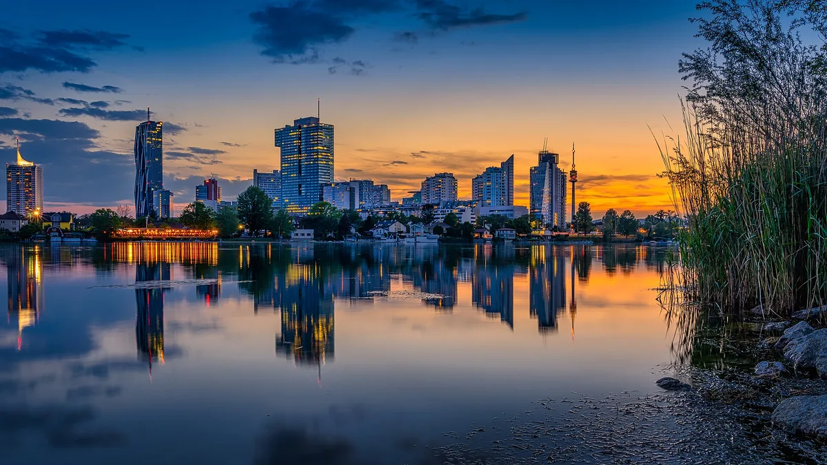 The Vienna skyline at sunset reflected in the Danube, with the DC Tower and Donauturm on the skyline
