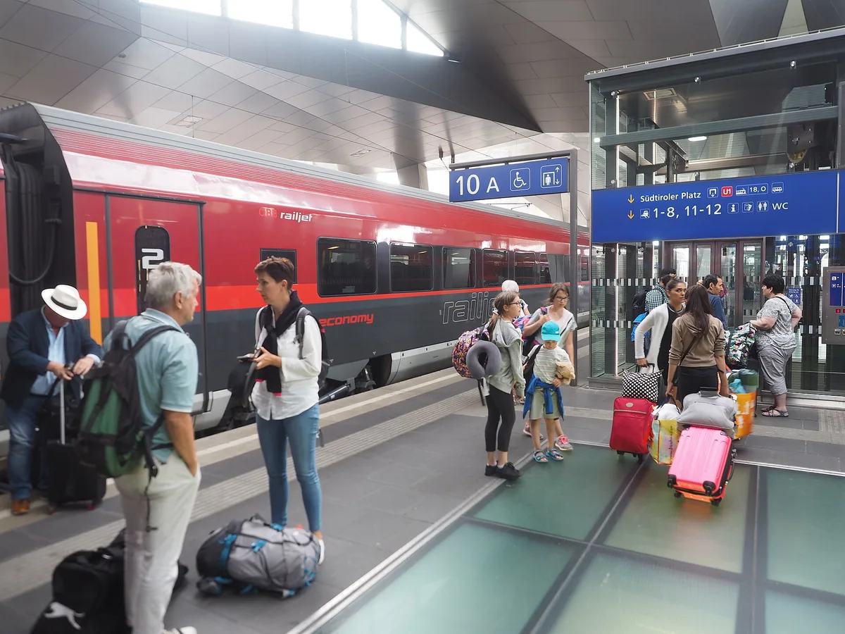 A red ÖBB Railjet train at a platform in Vienna Hauptbahnhof with passengers and luggage