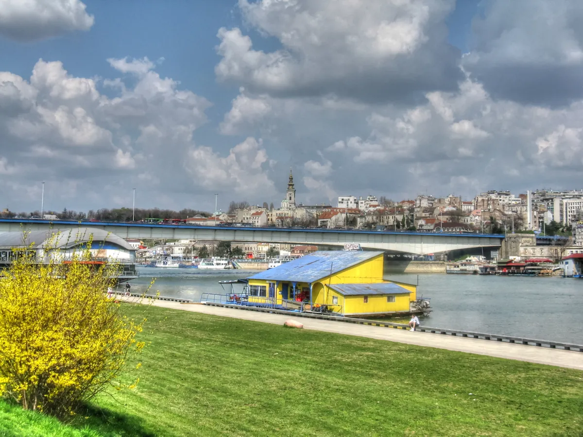 A yellow floating club moored on the Sava in Belgrade with the old town skyline and Branko bridge behind