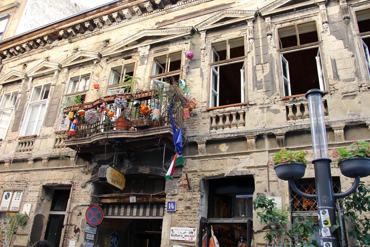 The crumbling facade of Szimpla Kert on Kazinczy street in Budapest, with plants on a rusting balcony above the entrance