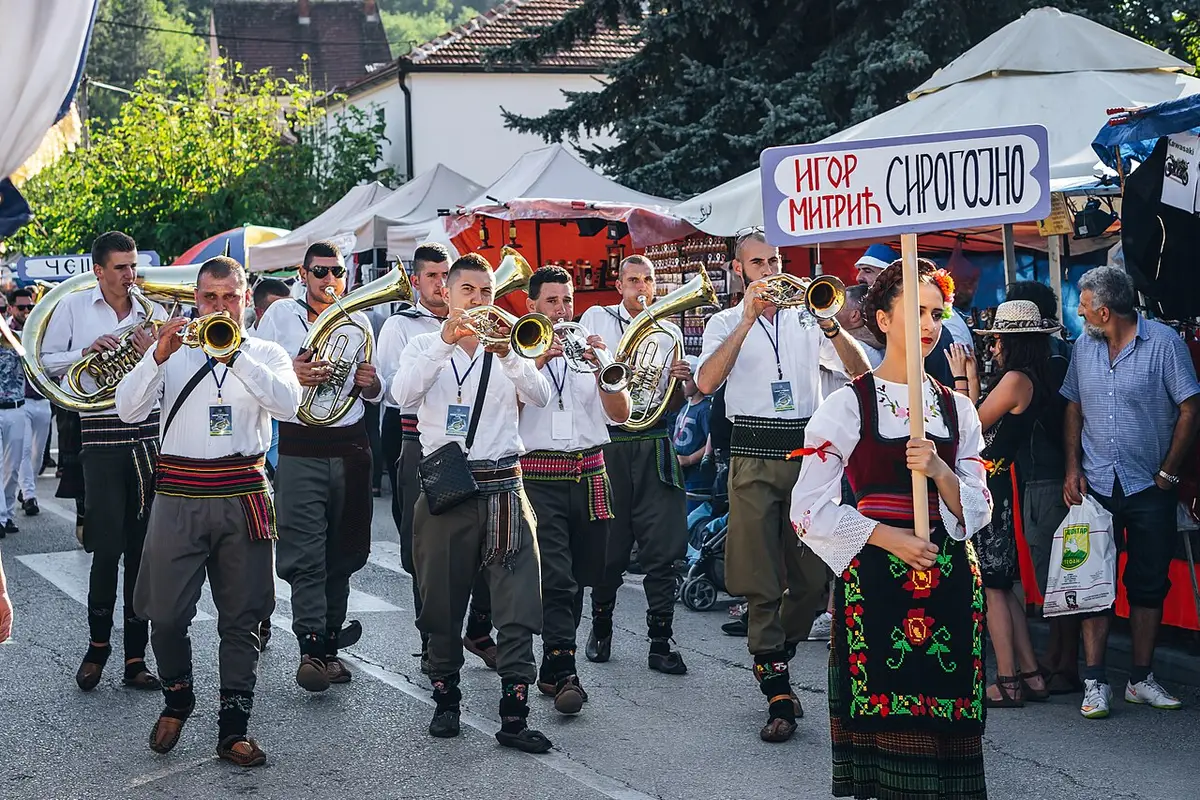 A brass band in white shirts and folk dress parading through the street at the Guča trumpet festival