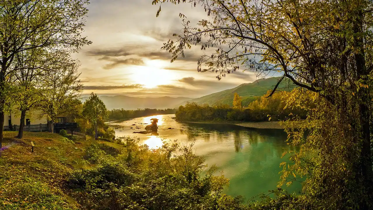 The small wooden house on its rock in the middle of the Drina river at golden hour, framed by autumn trees