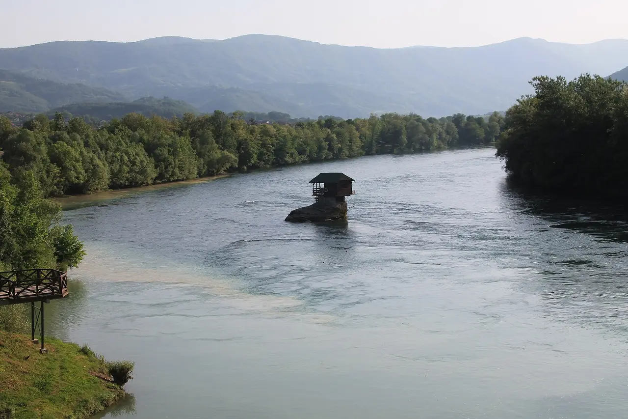 The wooden Drina house perched on a rock mid-river with green hills of the Drina valley behind
