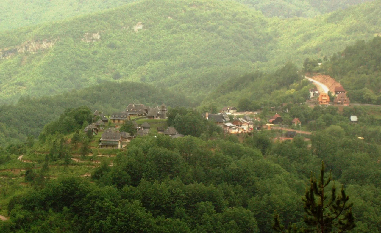 The wooden village of Drvengrad on its forested hilltop at Mokra Gora, timber houses clustered above misty green mountains