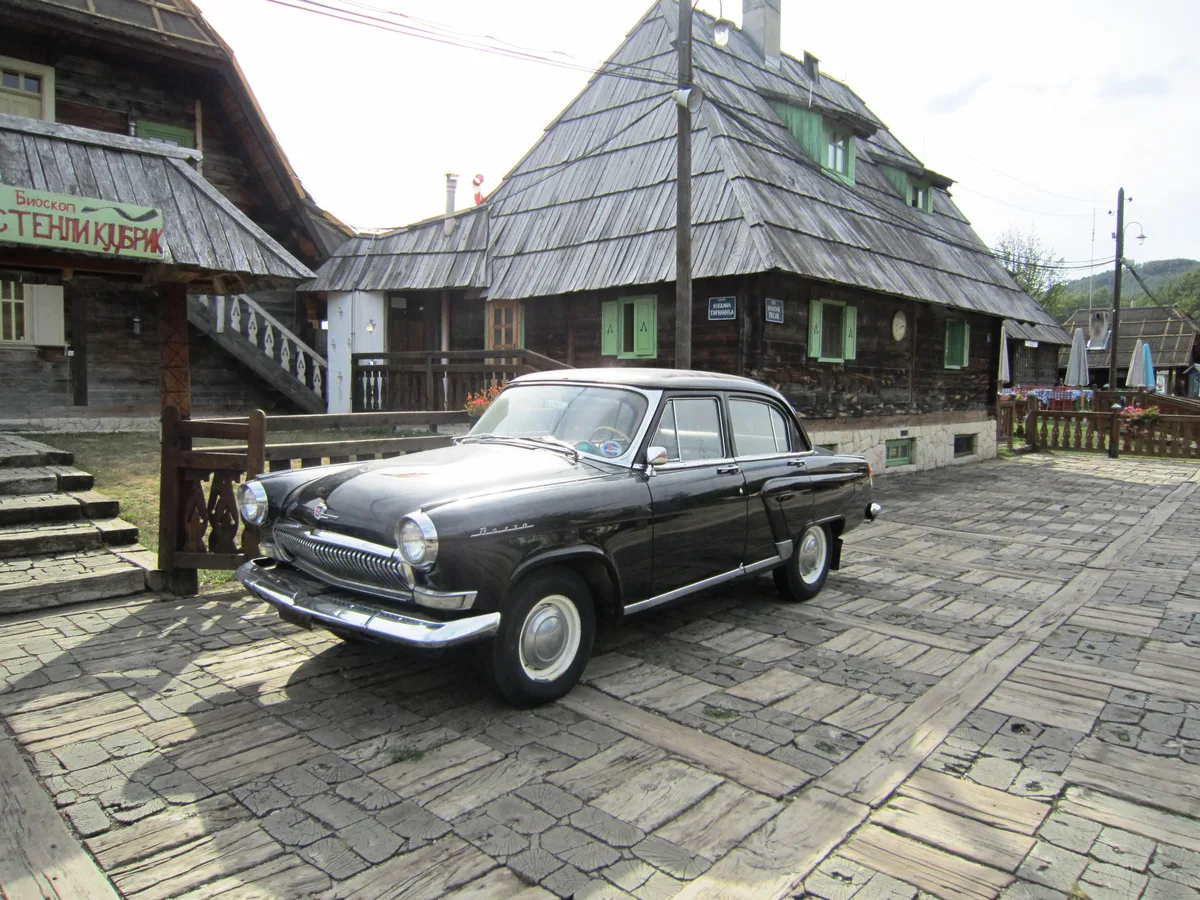 A vintage black car parked on the cobbles in Drvengrad in front of the Stanley Kubrick cinema and timber houses