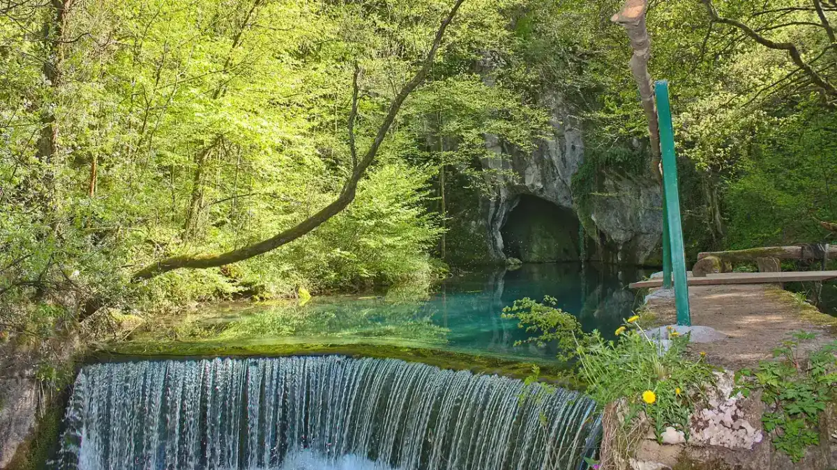 The turquoise pool and cave mouth of the Krupaj spring, ringed by green forest