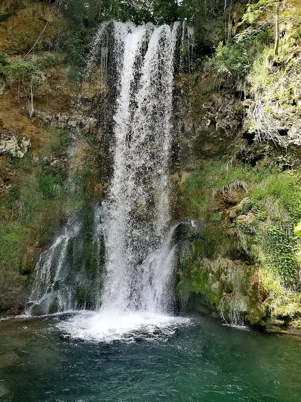 The tall Veliki Buk waterfall falling down a mossy tufa cliff into a green pool at Lisine