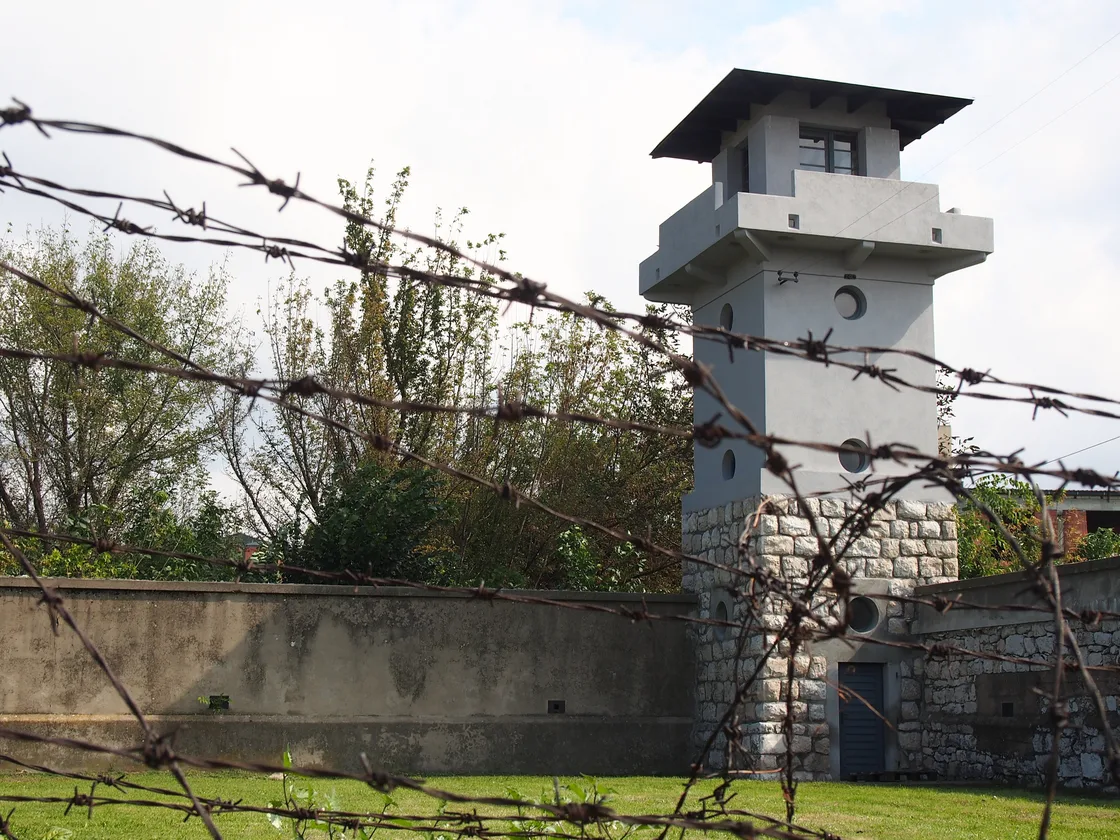 A restored watchtower and stone wall behind rusted barbed wire at the Crveni Krst concentration camp memorial in Niš
