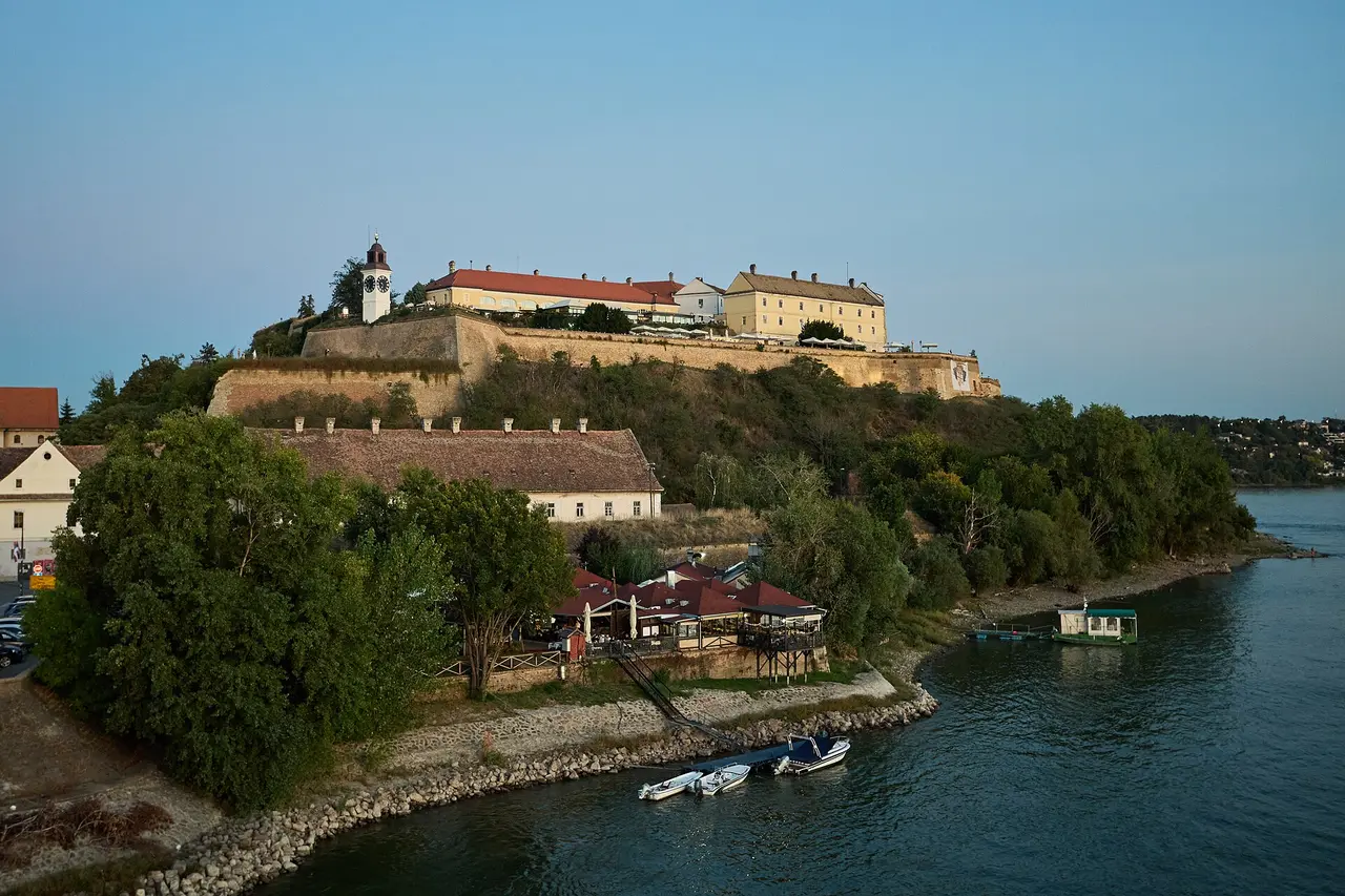The long yellow baroque barracks of the upper Petrovaradin Fortress under a bright sky, ramparts falling away toward the river