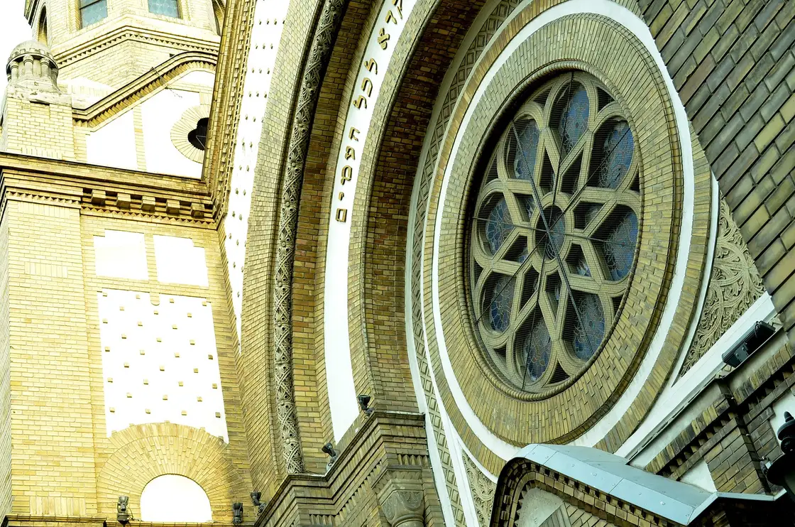 The ornate brick façade of the Novi Sad Synagogue with its large rose window and a Hebrew inscription above it