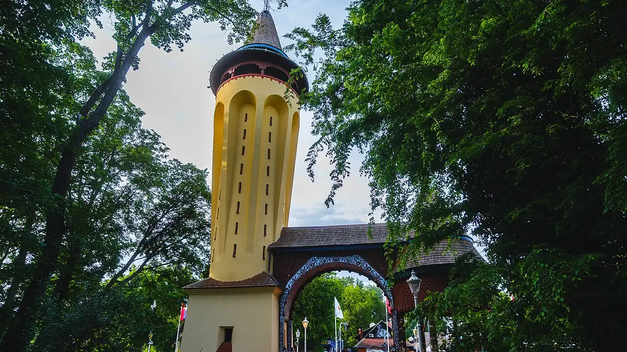 The restored yellow water tower at Palic with its ornamented timber gateway arch in front