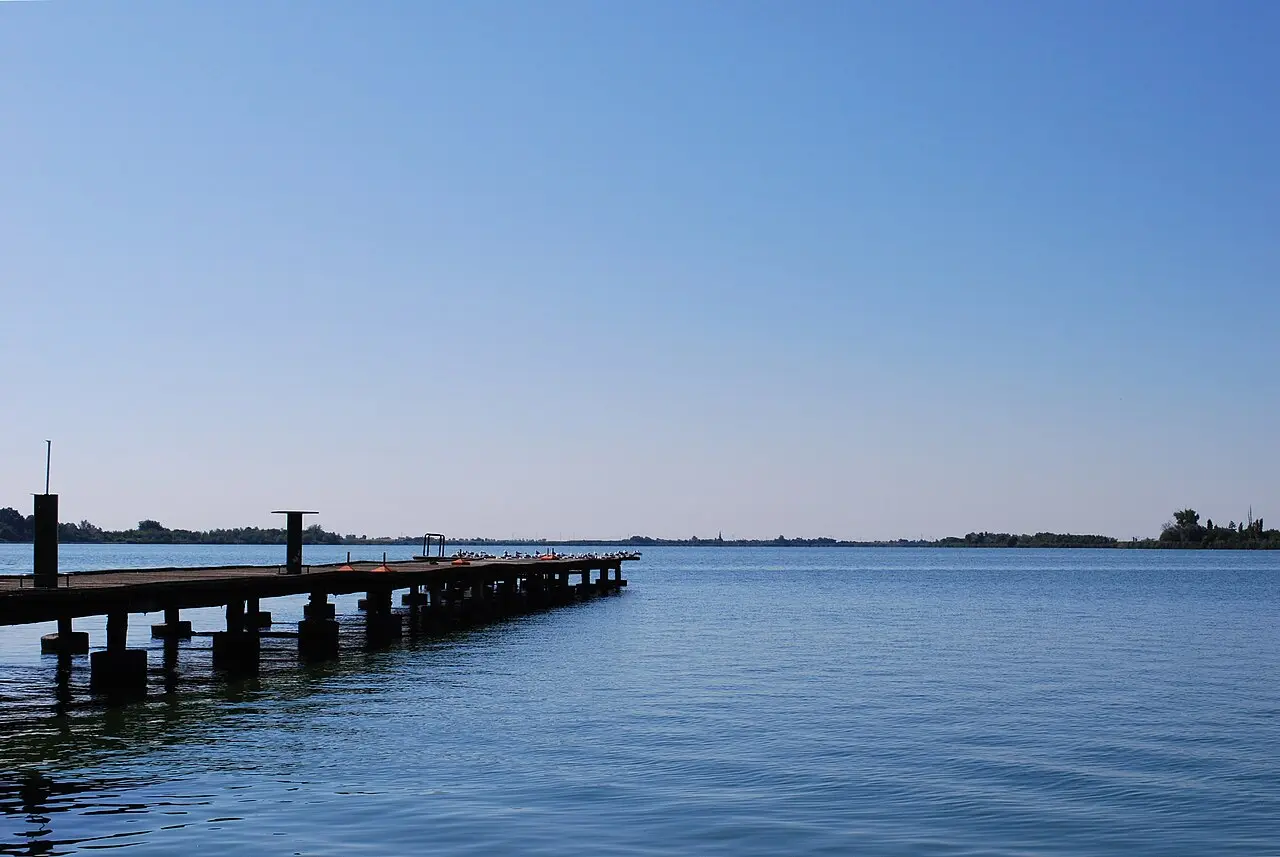 A concrete pier running out into the flat blue water of Lake Palic under a clear sky