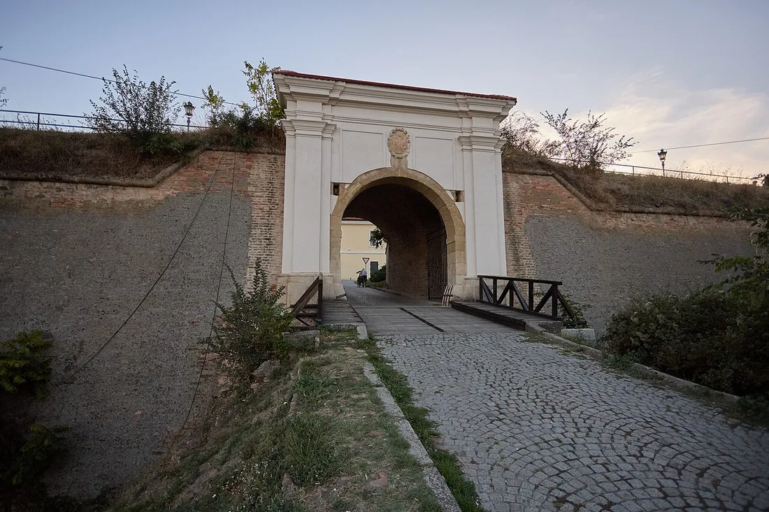 A baroque stone gate with a wooden drawbridge crossing the deep dry moat into Petrovaradin Fortress