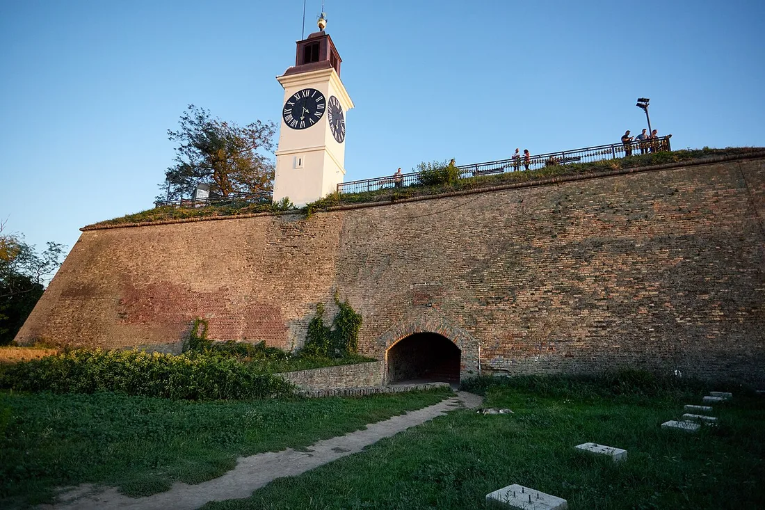 The brick ramparts of Petrovaradin Fortress rising to the clock tower, with a vaulted tunnel arch cut through the wall at the base