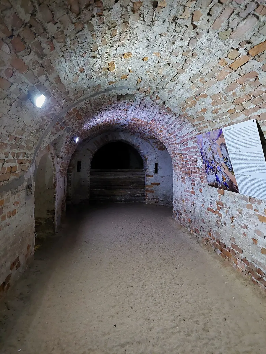 A brick-vaulted underground gallery inside Petrovaradin Fortress, dimly lit, with an exhibition panel on the wall