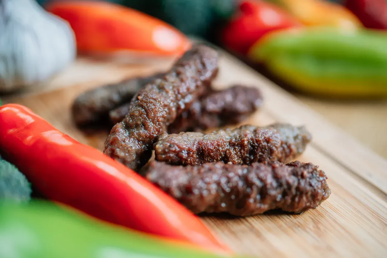 Close-up of grilled ćevapi with garlic and fresh peppers on a wooden board
