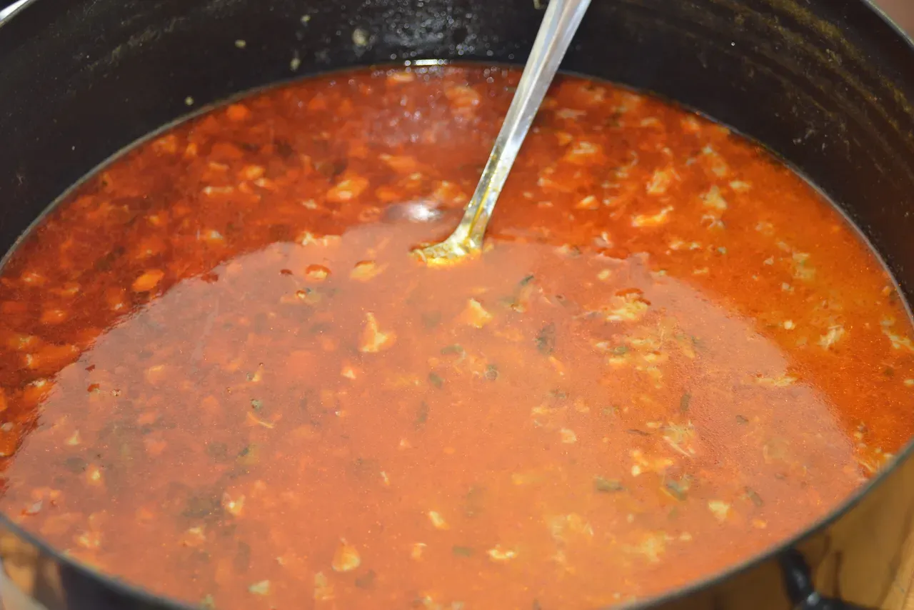 A cauldron of riblja čorba, the paprika-red Danube fish soup, being stirred with a ladle