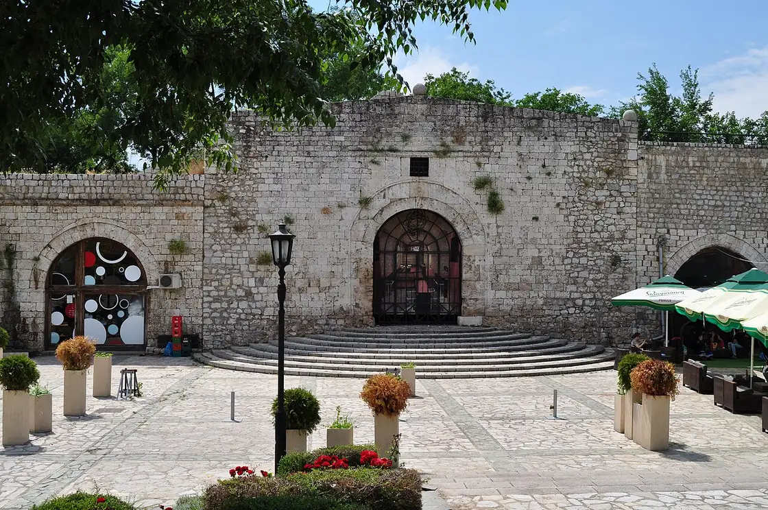 A stone gate and ramparts inside the Ottoman fortress of Nis in daylight, with café tables and planters on the flagstones