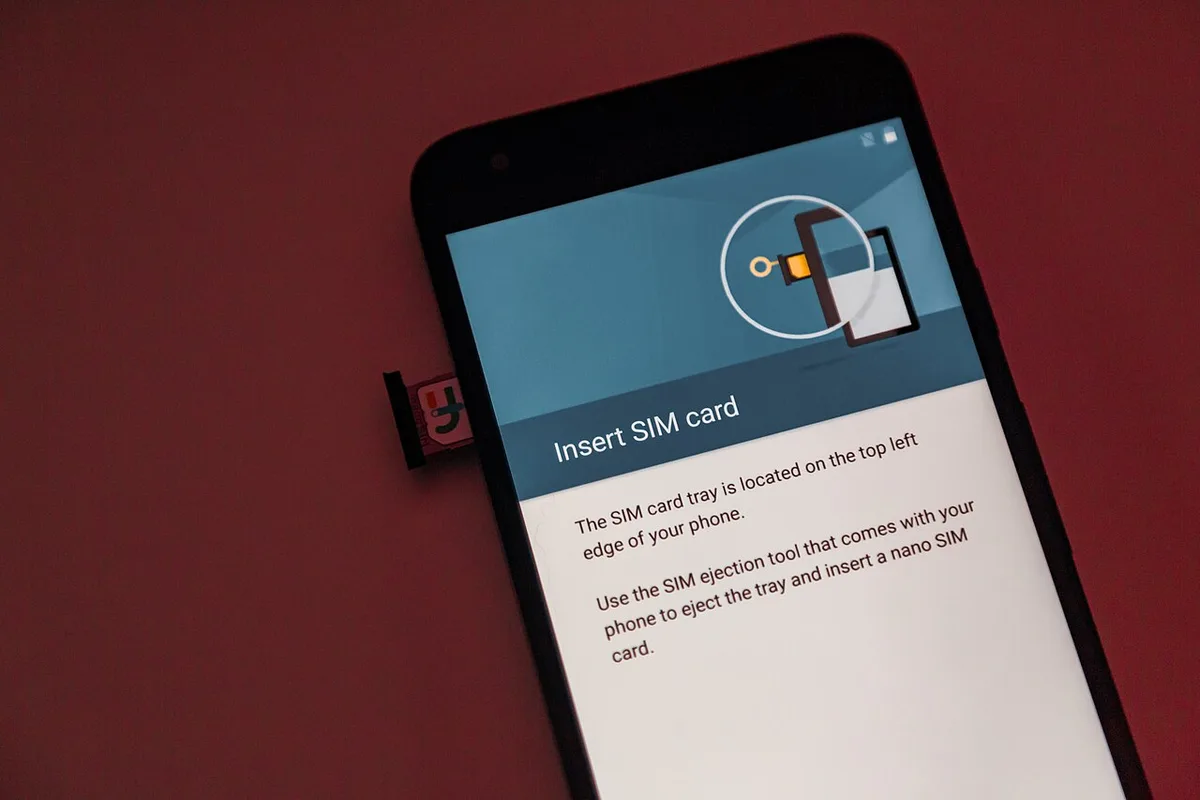 A hand sliding a nano SIM card into the tray of a smartphone