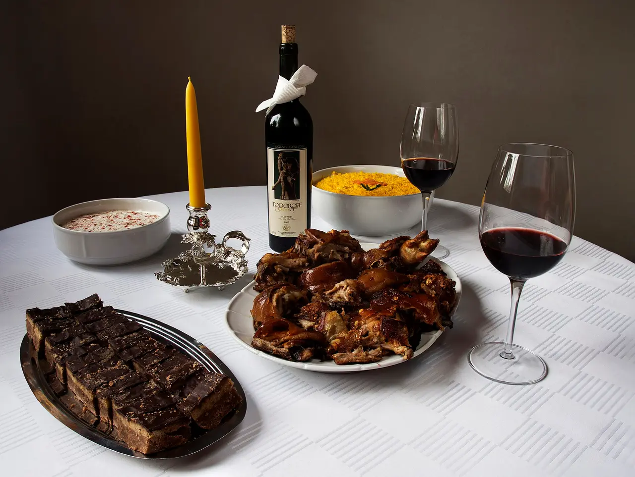 A Serbian Christmas table with roast meat, cesnica bread, a candle and two glasses of red wine