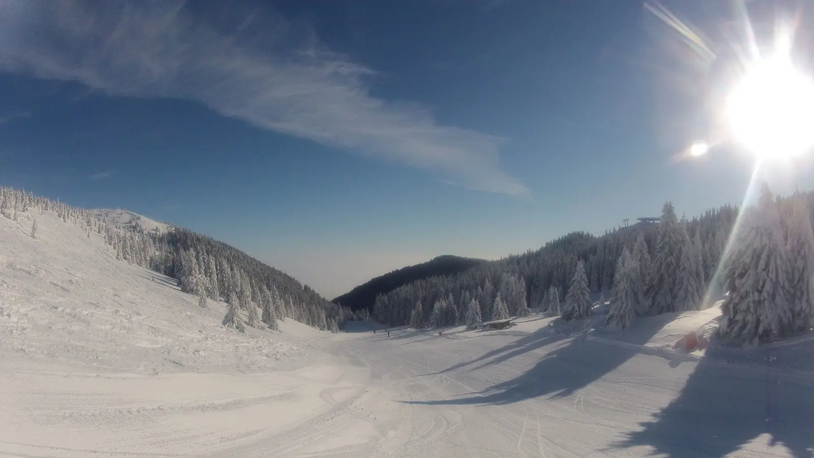 A groomed red run on Kopaonik under a bright winter sun, with frost-covered spruce down both sides of the piste