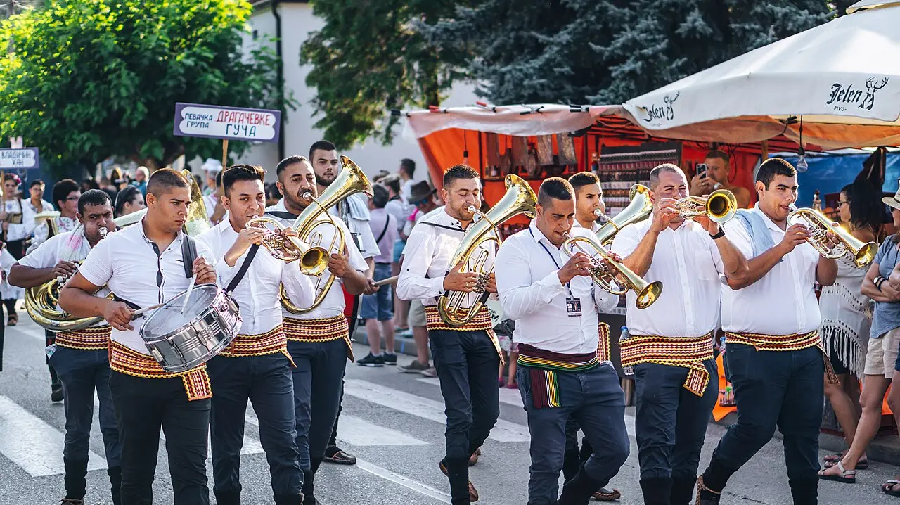 A brass orchestra in white folk shirts playing trumpets in the street at the Guča festival, a drummer alongside them