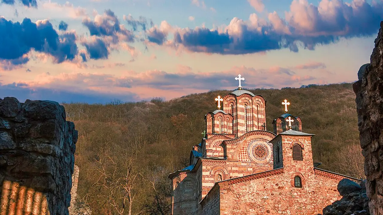 The banded stone domes of Ravanica monastery at dusk, framed by the ruined fortress wall around it