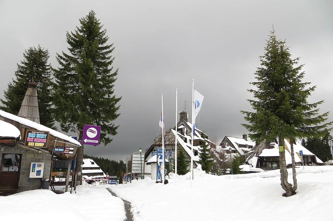 The base of Kopaonik ski resort in winter, with ski rental shops and wooden chalet roofs under fresh snow
