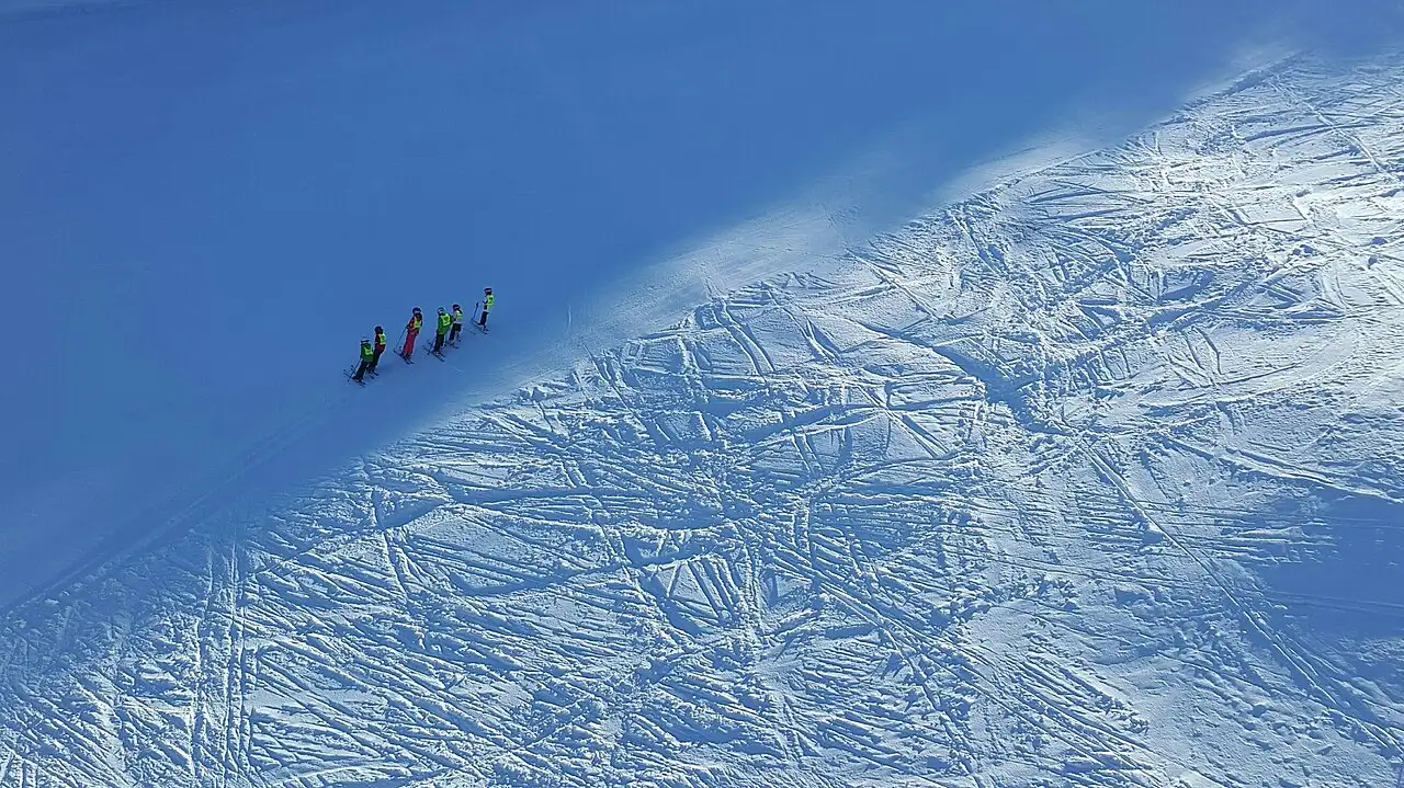 A line of ski school pupils in bright jackets on a groomed piste at Tornik above Zlatibor