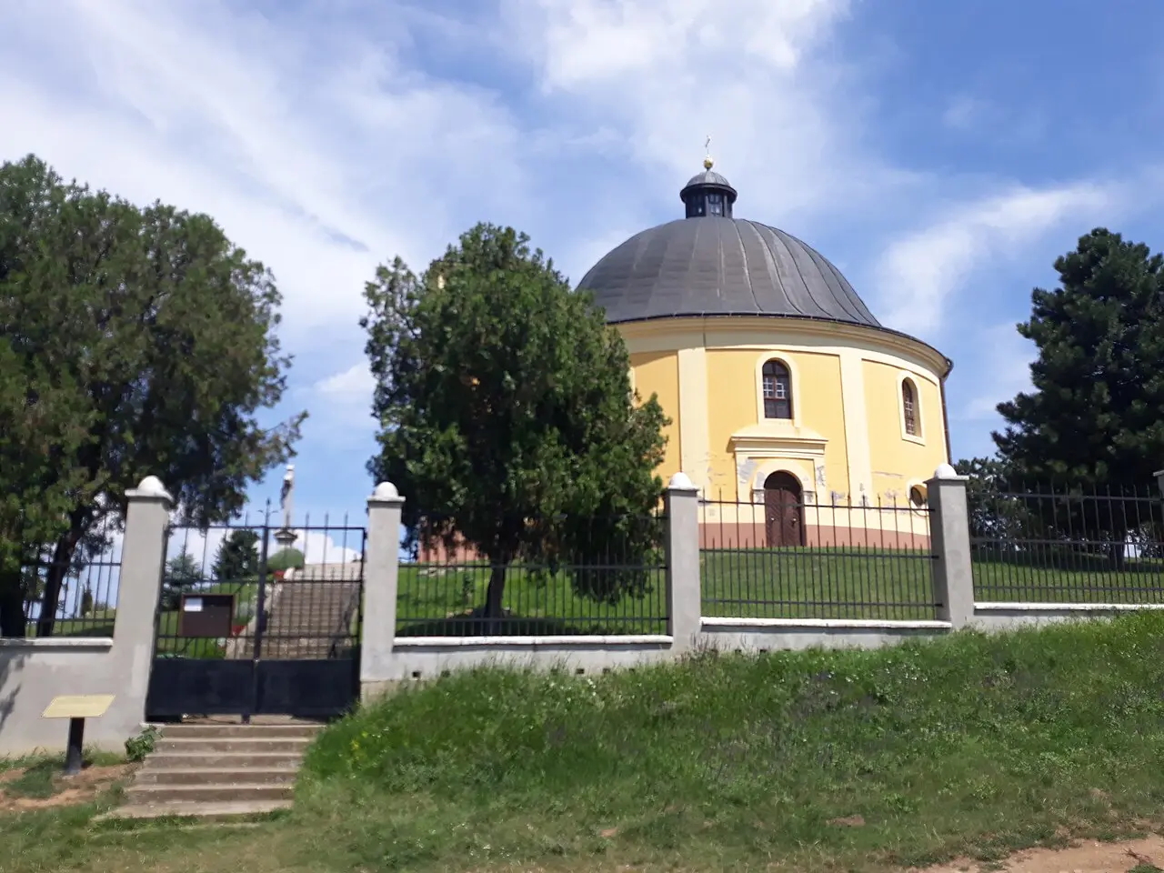 The round yellow Chapel of Peace with its dark dome standing on a grassy hill behind a fence