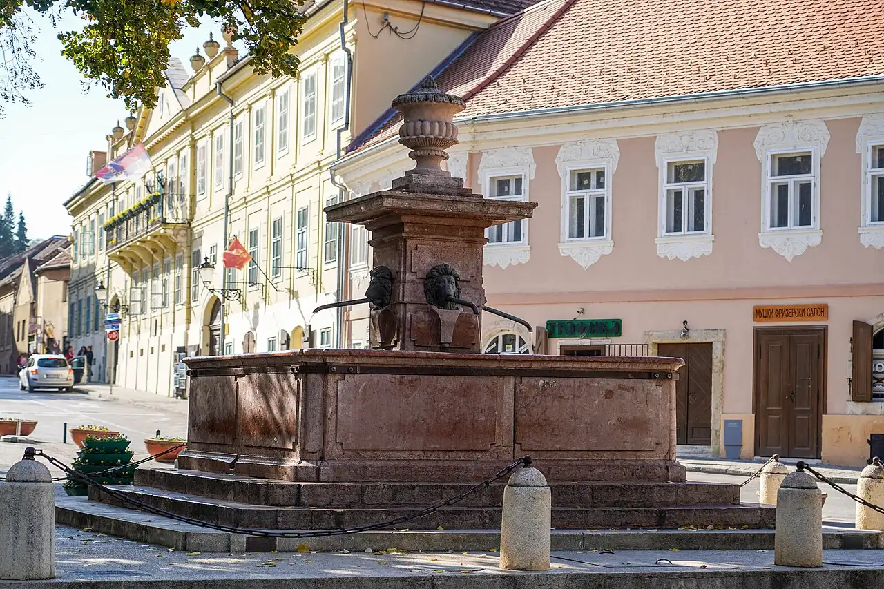 The red stone Four Lions Fountain in Sremski Karlovci with Baroque houses behind it
