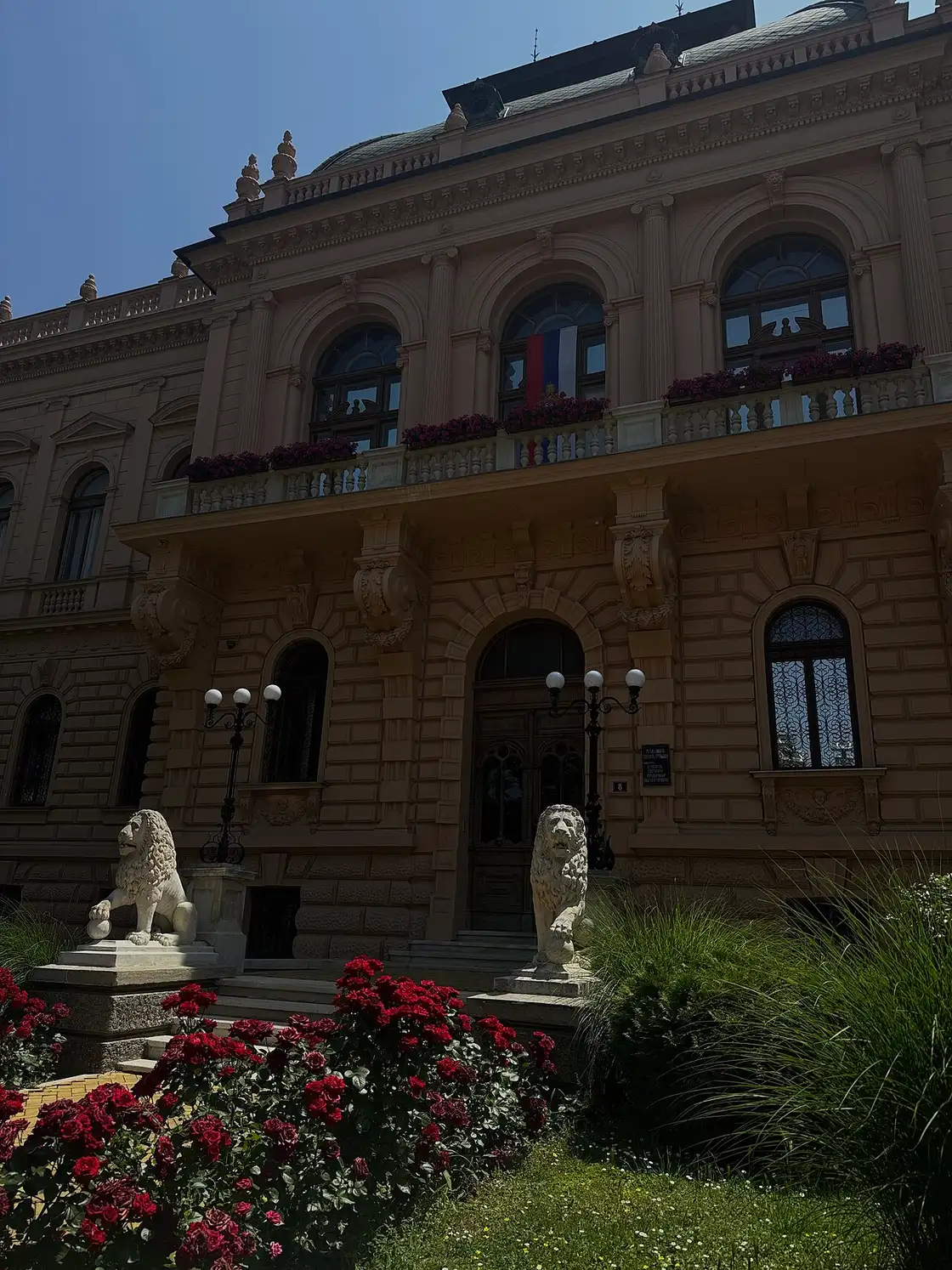 The ornate facade of the Patriarchal Court in Sremski Karlovci with two stone lions flanking the entrance and roses in front