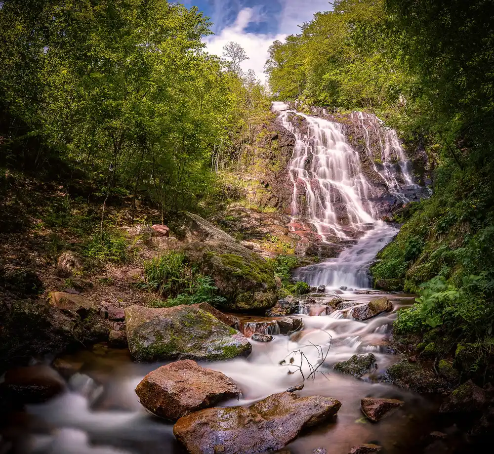 The tall Pilj waterfall dropping through green forest over dark rock above the village of Topli Do