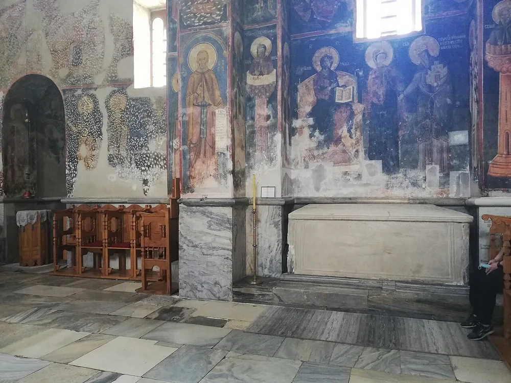 The white marble tomb of Stefan Nemanja set against frescoed walls inside the Church of the Virgin at Studenica