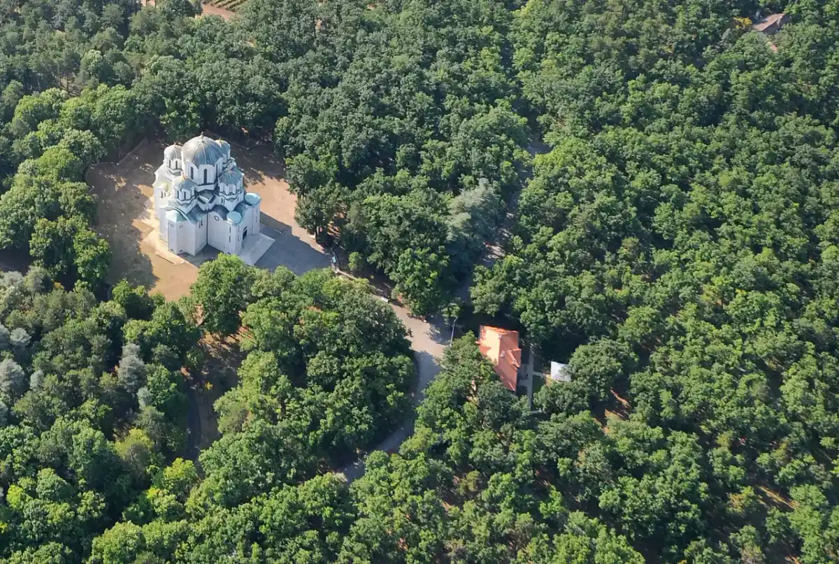 Aerial view of the white marble domes of the Church of St George at Oplenac surrounded by forest