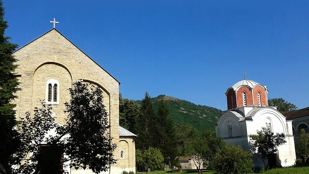 The white marble Church of the Virgin and the domed King's Church at Studenica monastery below a wooded hill