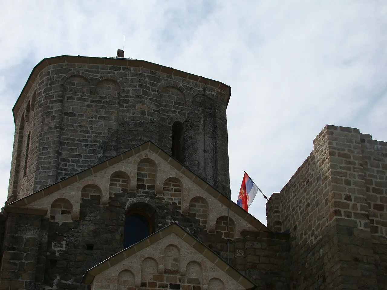 The stone tower and dome of Djurdjevi Stupovi monastery with a Serbian flag on the wall