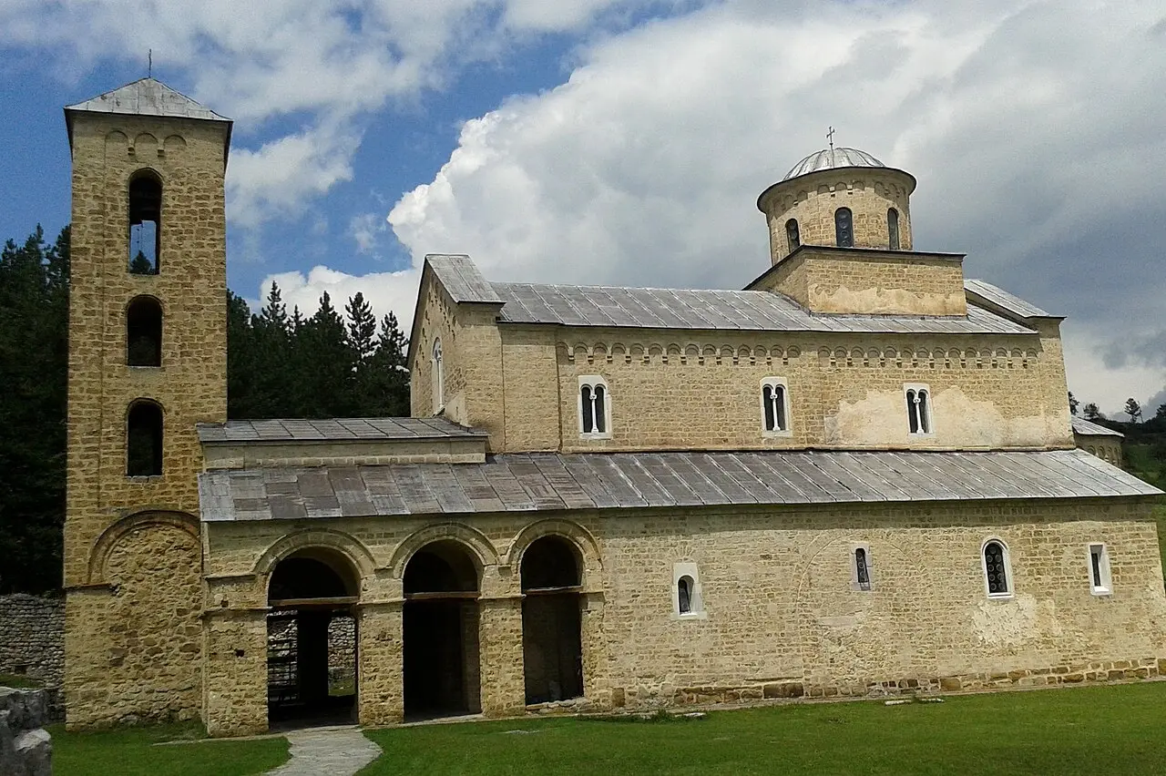 The plain stone church of Sopocani monastery behind its low wall in green hills